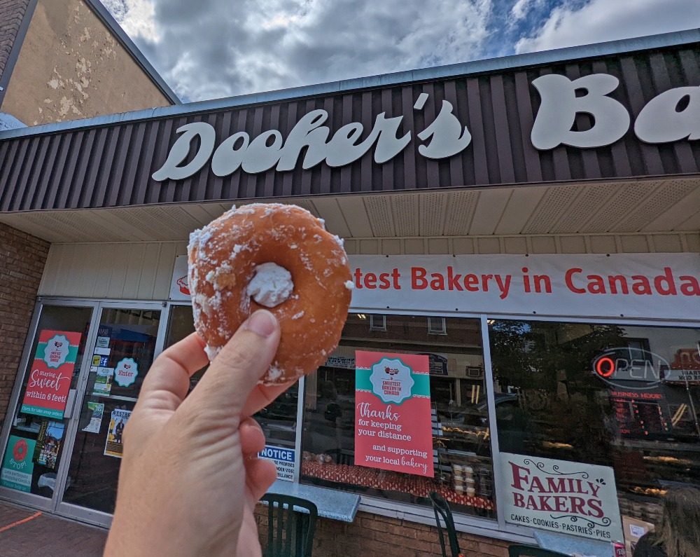 Hand holding up a cream filled donut in front of Dooher's Bakery
