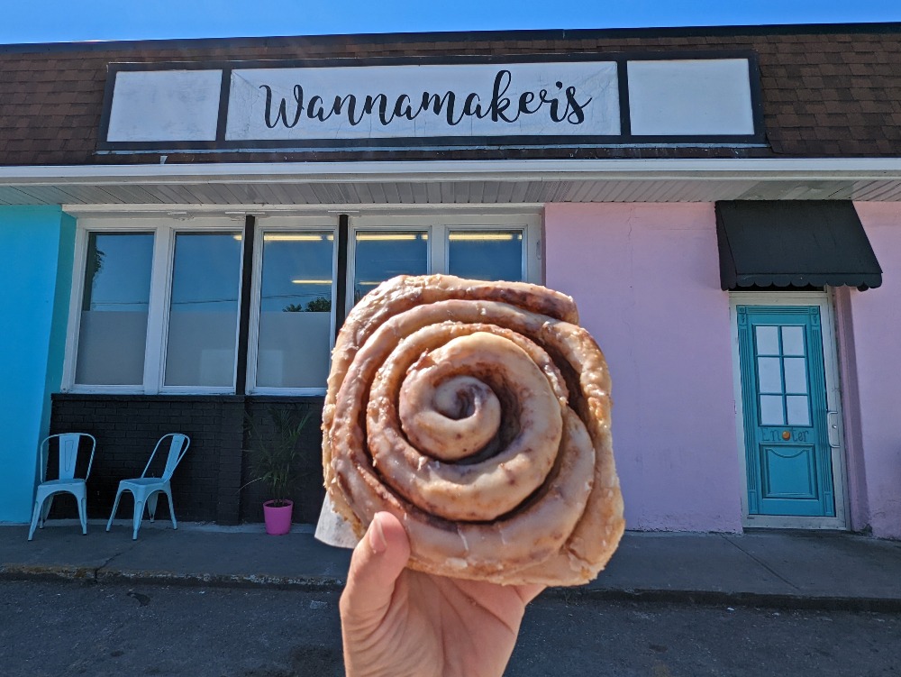Hand holding up Wannamaker's cinnamon bun in front of the store