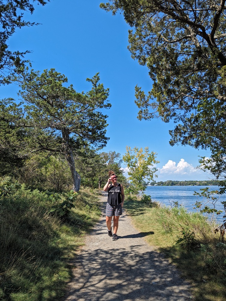 Me hiking along a trail in Massassauga Point Conservation Area. The trail has forest to one side and water to the other.