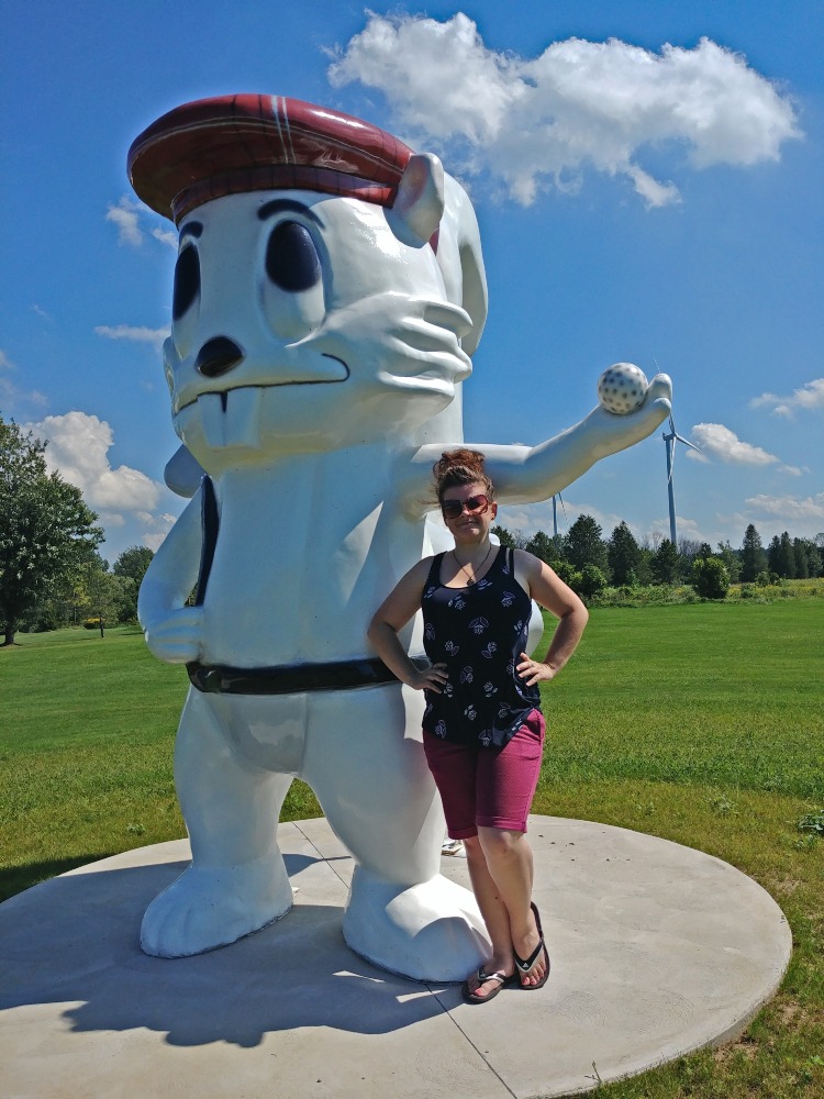 Me standing next to a big white squirrel statue that is holding a golf bag and has a golf cap on his head.
