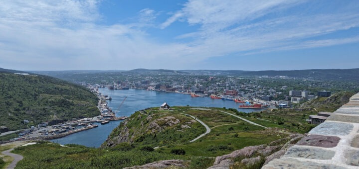 View of St. John's from Cabot Tower, with rolling grassy hillsides leading to St. John's Harbour with the city beyond it.