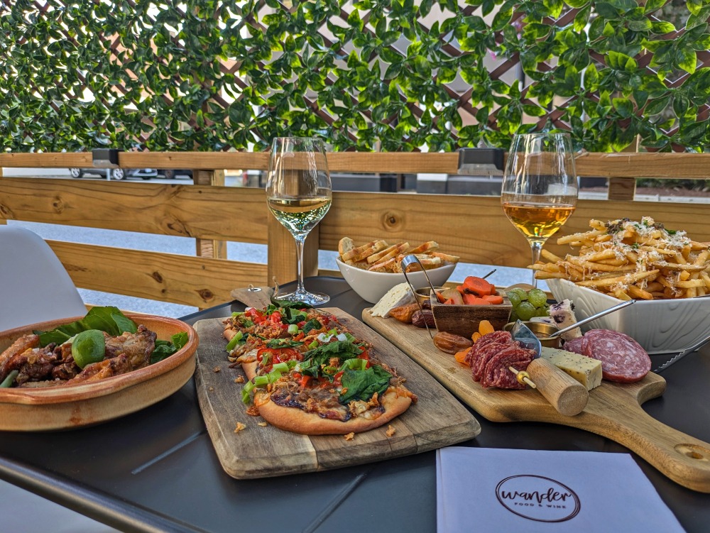 Table full of food including charcuterie board, wine glasses, fries and flatbread with a napkin with the name of the restaurant, Wander Food & Wine