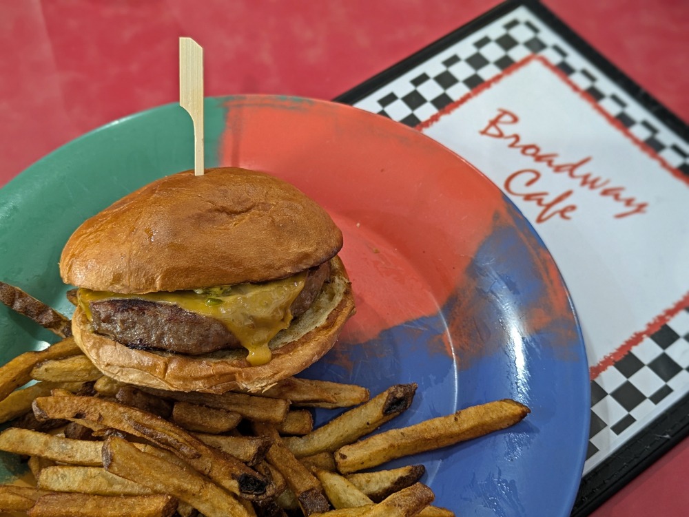Plate full of French fries topped with a cheese burger on top of the Broadway Cafe menu