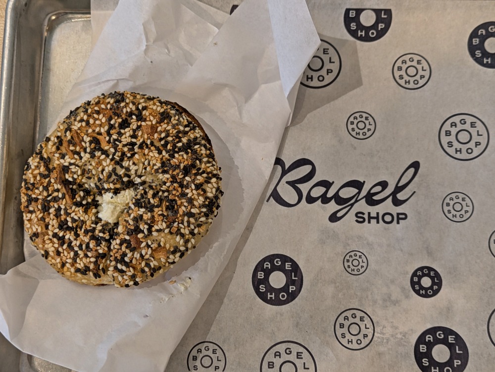 Everything bagel with cream cheese on a tray at Bagel Shop