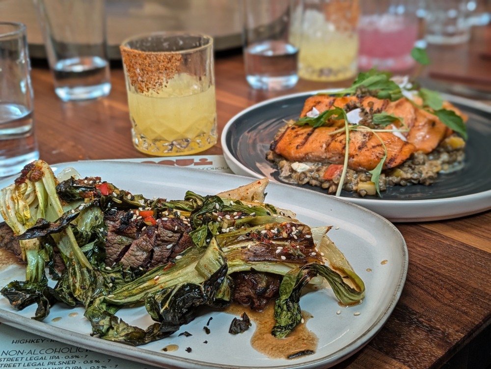 Steak ant fish dishes at Loqui restaurant with cocktails in the background