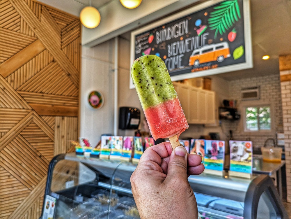 My hand holding up an ice pop in Papaya Pops, a colourful shop selling iced popsicles.