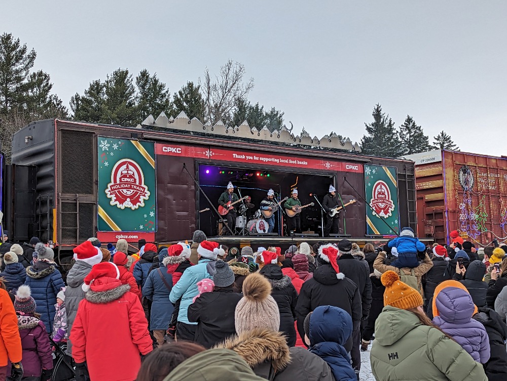 CPKC Holiday Train with band playing inside and crowd of people out front.