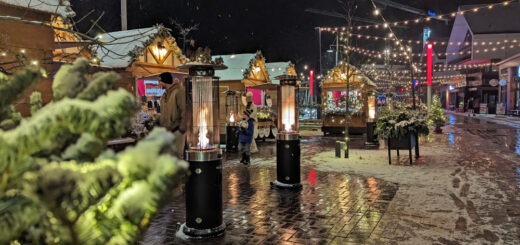 Winter scene of Christmas market stalls with lights strung up at night.