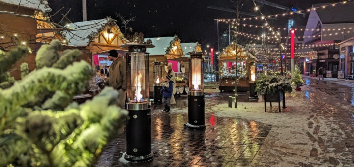 Winter scene of Christmas market stalls with lights strung up at night.