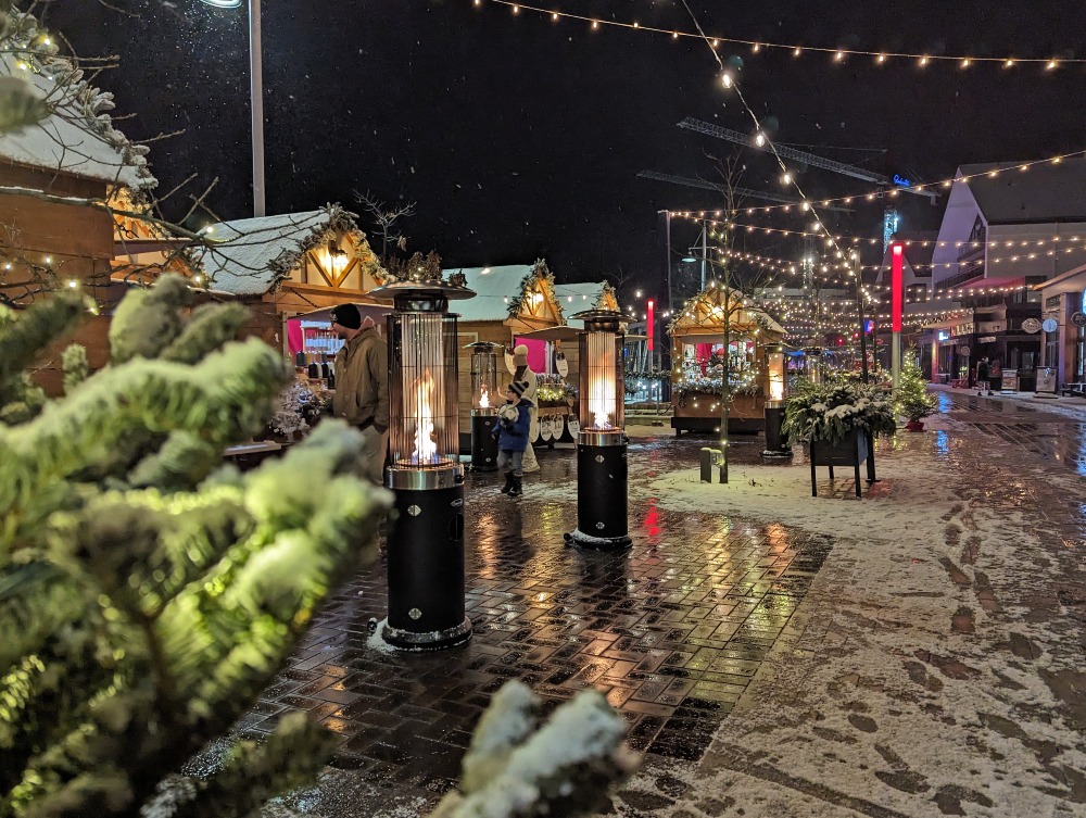 Winter scene of Christmas market stalls with lights strung up at night.