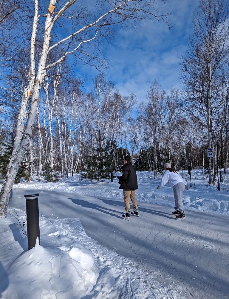 Nina's Way Skate Trail at Kivi Park. The outdoor skating trail is lined by forest and has two people skating on it