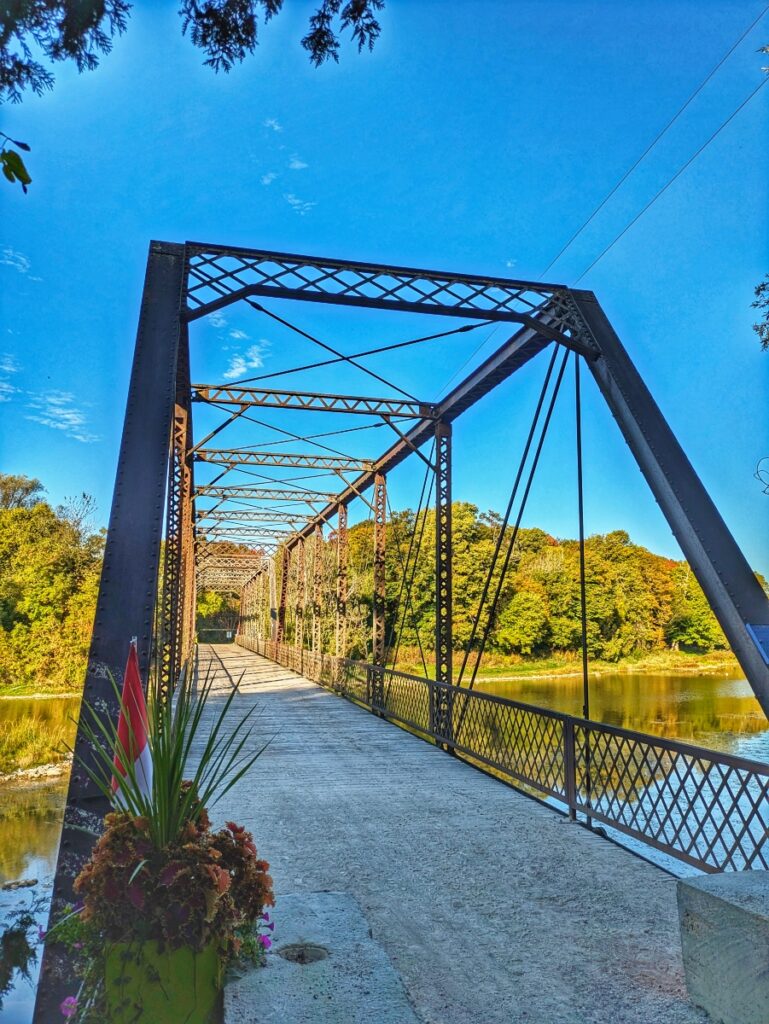iron bridge, known as Ball's Bridge, in Huron County. Metal is contrasted with clear blue sky and dense forest on the other side of the Maitland river.