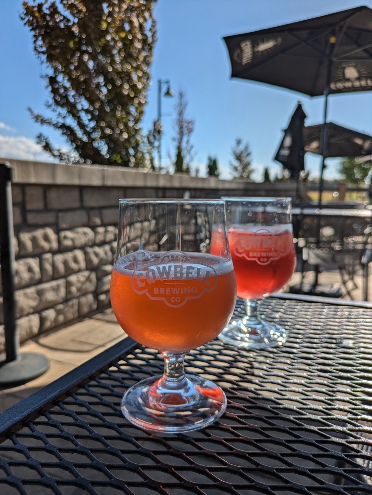 Two glasses of ciders on a patio table at Cowbell Brewery