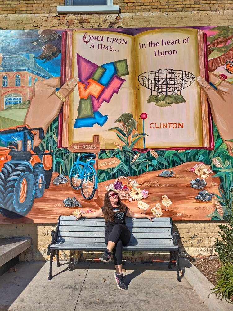me sitting on a bench in front of a mural in Clinton