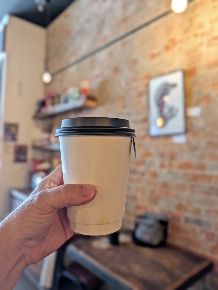 Hand holding up a coffee at Cork and Bean coffee shop in Peterborough