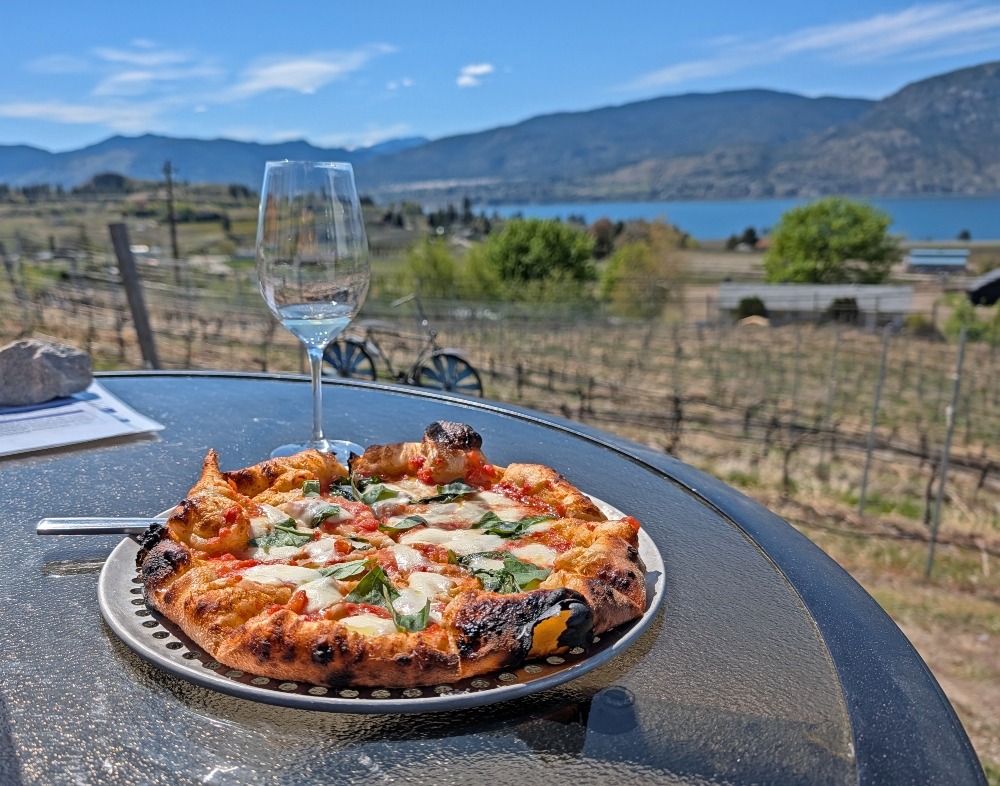 Pizza and glass of wine at Chain Reaction Winery in Penticton. The view is of the lake and mountains