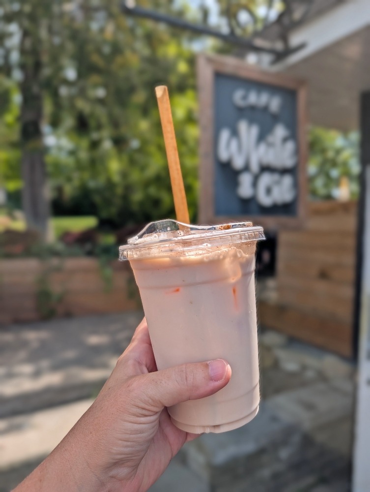 Hand holding up an iced latte in front of Hand holding up an iced latte in front of Cafe White & Compagnie