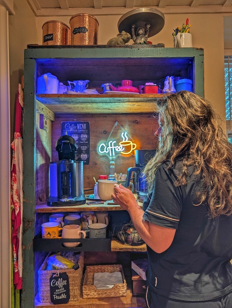 Me standing in front of the coffee station at the Old Mill Manor, holding a mug