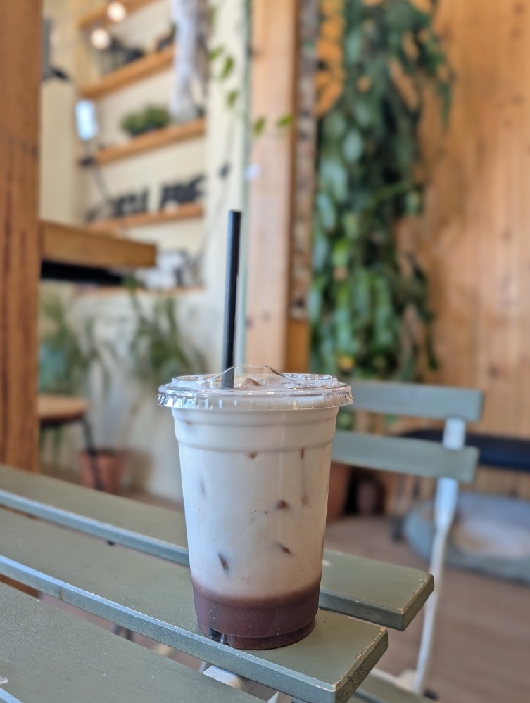 Iced latte at Café La Petite Voisine sitting on a wooden table with plants behind it