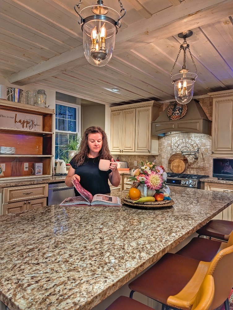me holding a mug and reading a cookbook in the kitchen at the Old Mill Manor