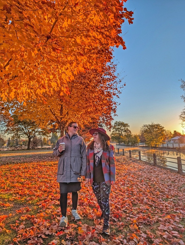Friend and I walking along the Rideau Canal in Smiths Falls in the fall. There are trees with orange leaves to one side and lots of leaves on the ground