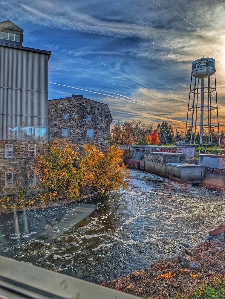sunset view from The Lockmaster's Taphouse in the fall with an old mill, waterfall and water tower with trees around